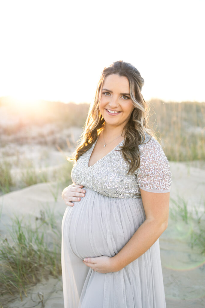 first time mom smiling and holding her pregnant belly during virginia beach maternity portraits