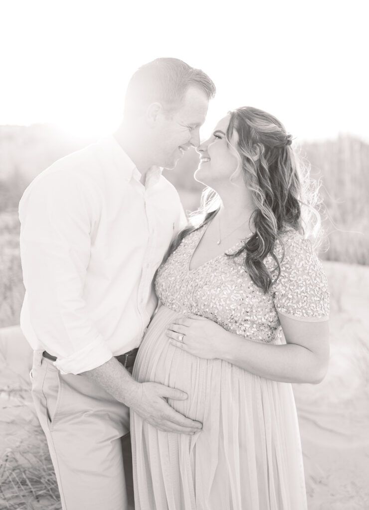 couple smiling and snuggling during virginia beach maternity photos