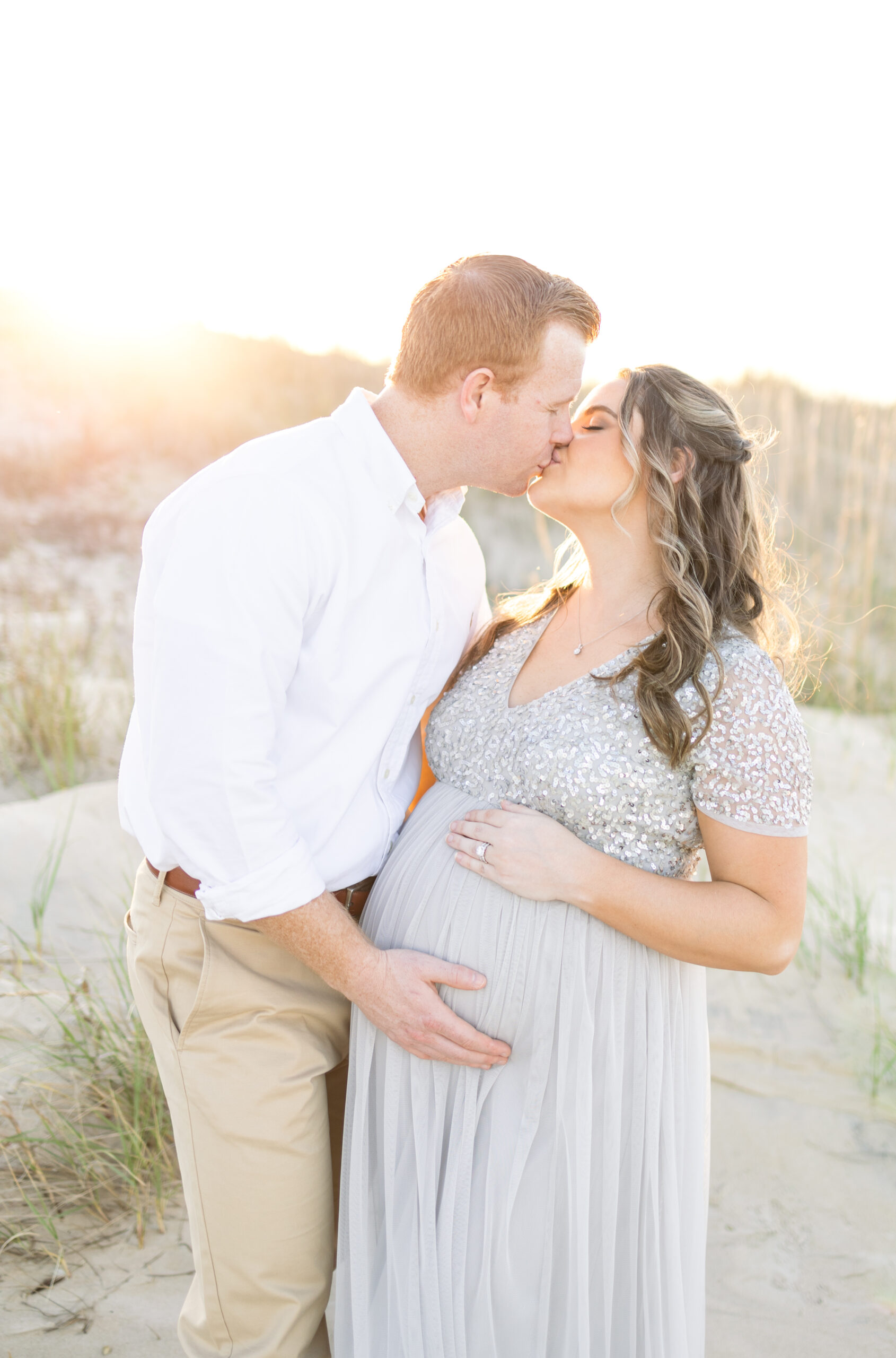 maternity portraits of mother and father hugging and kissing on the beach in virginia beach