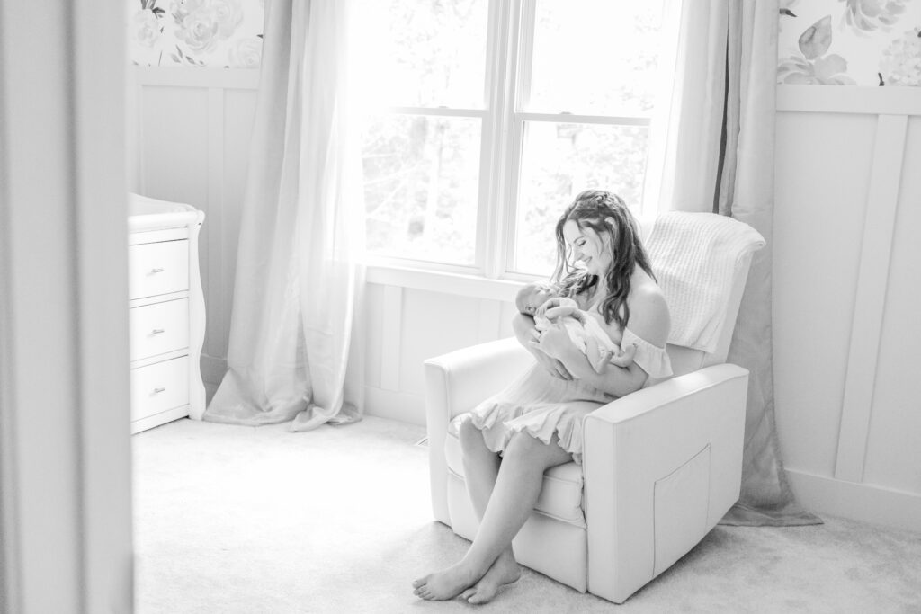 new mother smiling down at her baby girl in virginia beach nursery during newborn photo session