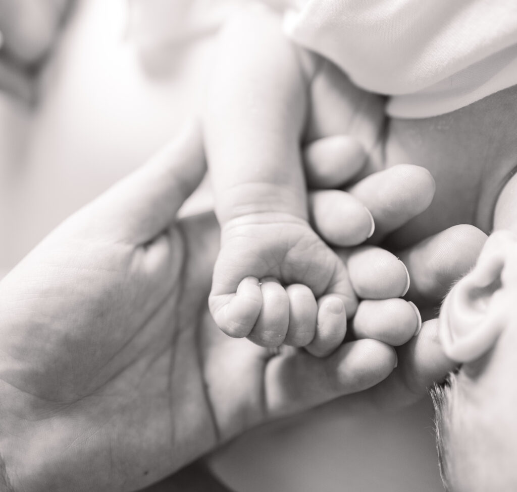 black and white image of newborn baby hand in mom and dads hand during newborn photos 
