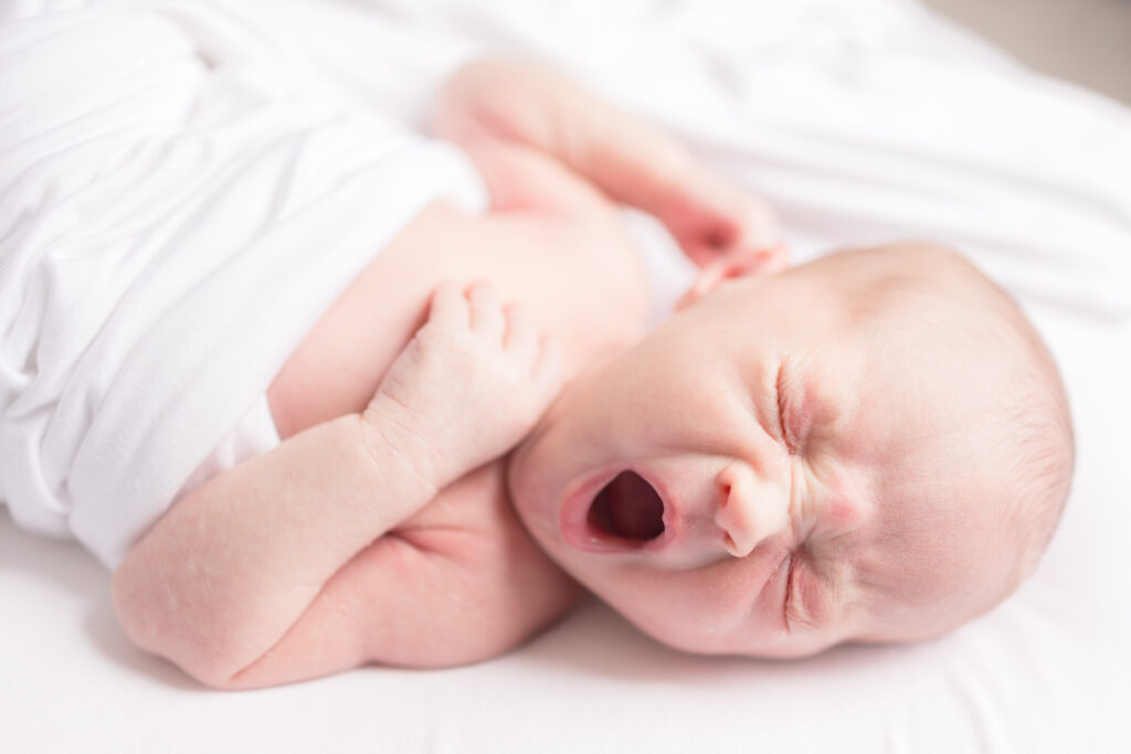 newborn lifestyle session image of baby girl yawning and stretching in nursery 

