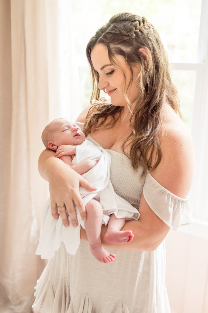 mother smiling down at newborn baby girl during in-home newborn photos in virginia beach