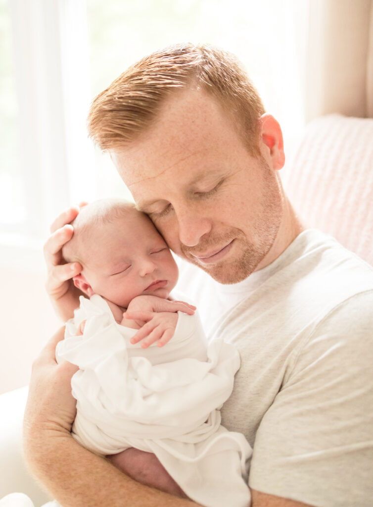 dad holding newborn baby girl and smiling in the nursery during lifestyle newborn photos in virginia beach