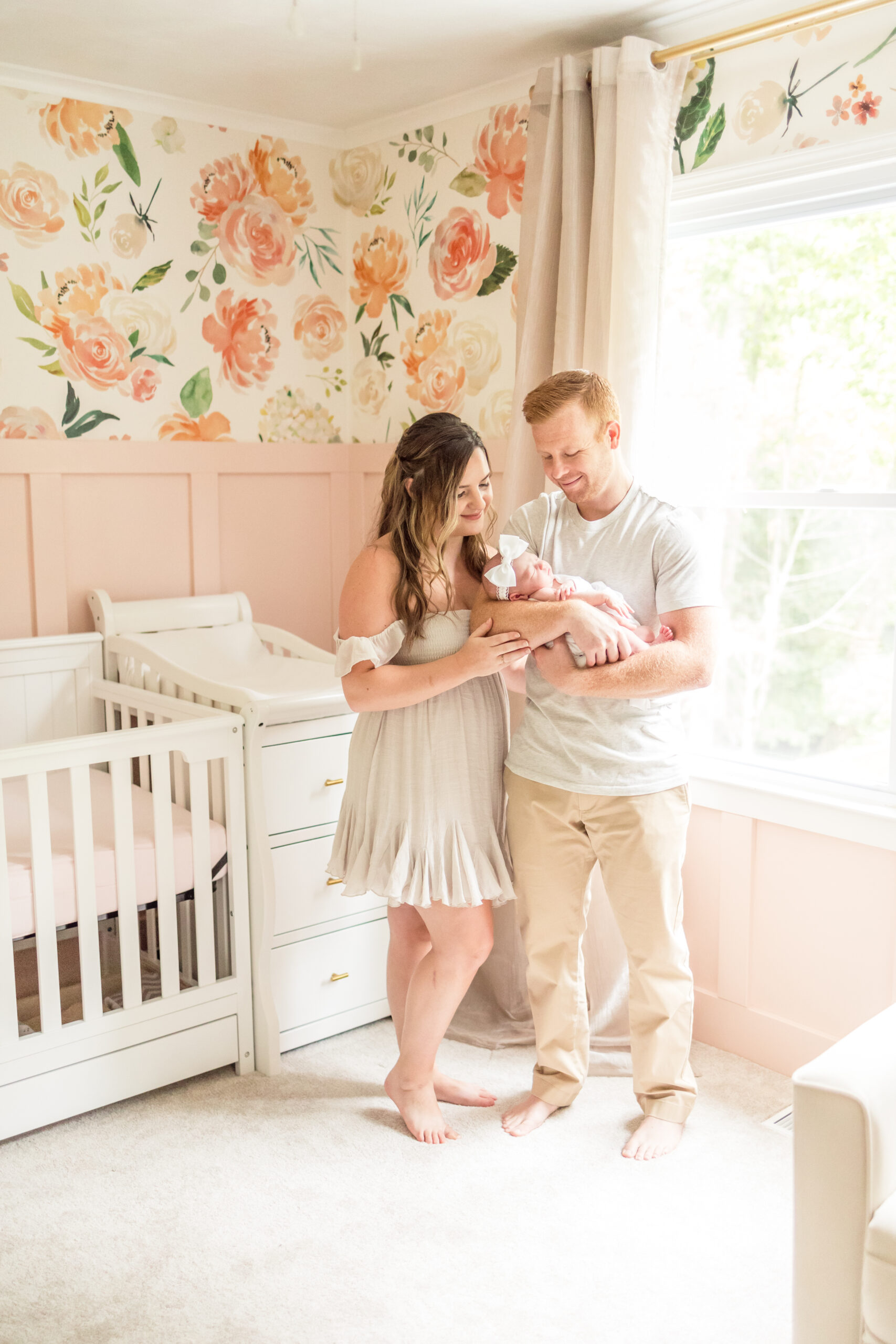 mom and dad smiling at newborn baby girl during their in-home newborn session in virginia beach in pink floral nursery