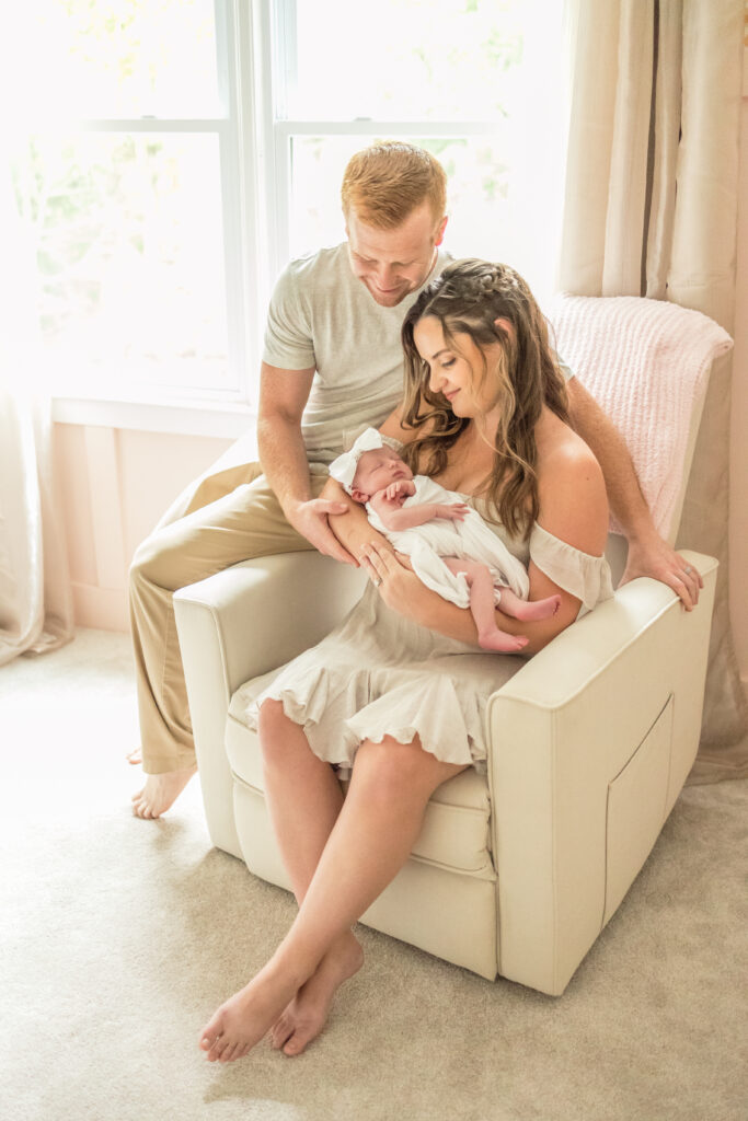 lifestyle newborn photos in baby's nursery in virginia beach showing mother, father and newborn baby girl snuggling up in nursery