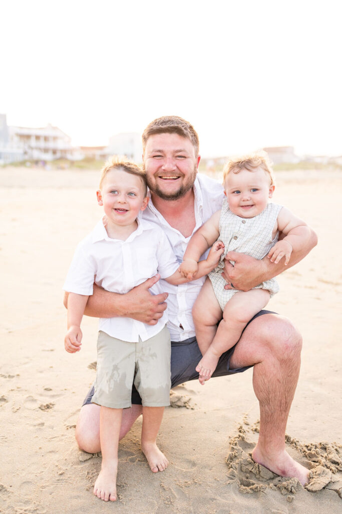 dad holding his two sons and smiling for the camera during virginia beach family portraits