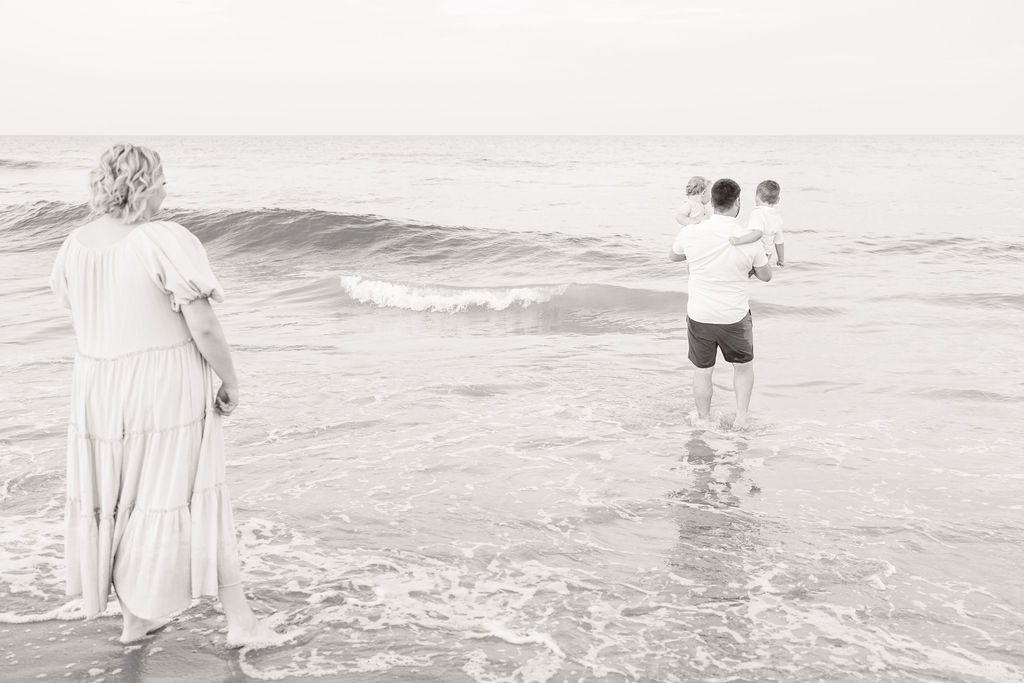 mom watches dad carrying young sons into the ocean during family photos in virginia beach