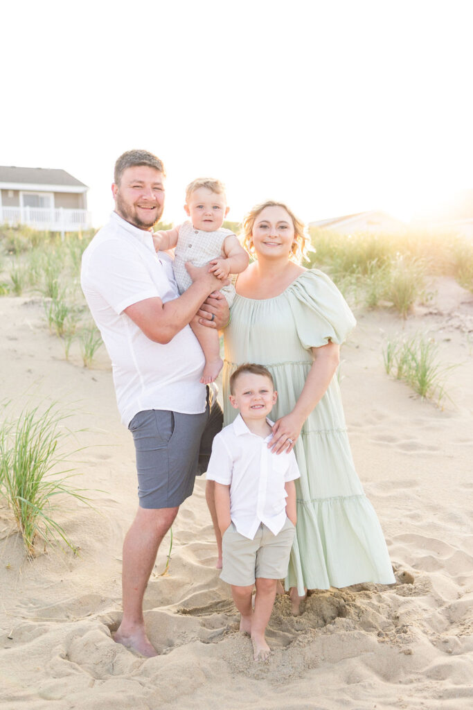 family of 4 smiling on the beach for their annual family photos in virginia beach