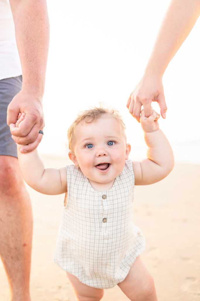 adorable baby boy walking while holding hands with his mom and dad during sunset photos in virginia beach