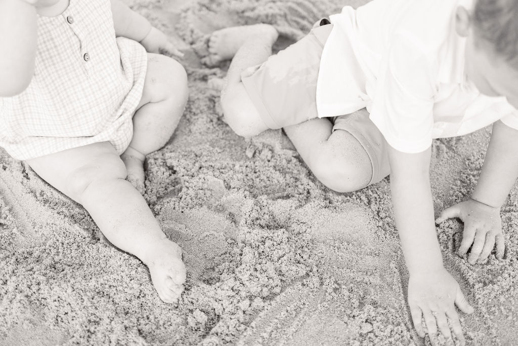 baby and toddler playing in the sand on the beach, this photo depicts a detail photo of their hands and feet in the sand 