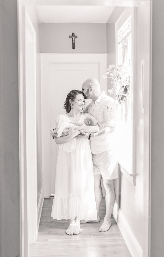 first time mother and father snuggling with baby and kissing during at home newborn photos