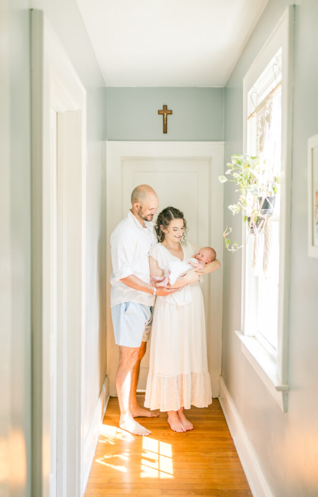 lifestyle newborn photos at home in virginia beach, virginia with mom and dad holding baby boy and smiling down at him. 