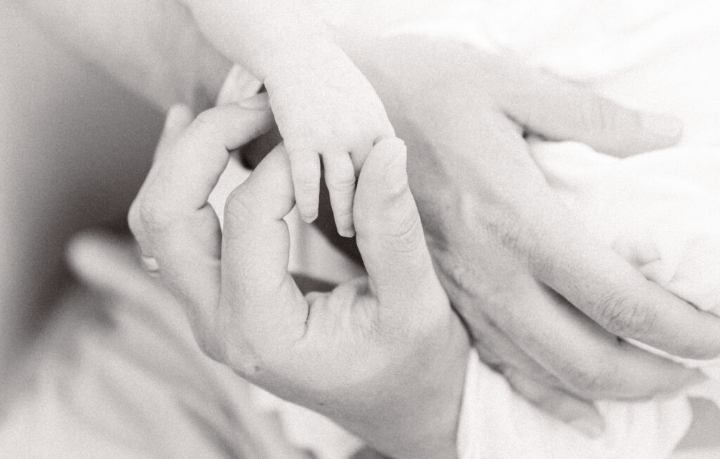 dad holding newborn baby boy's hand during newborn photos at home 