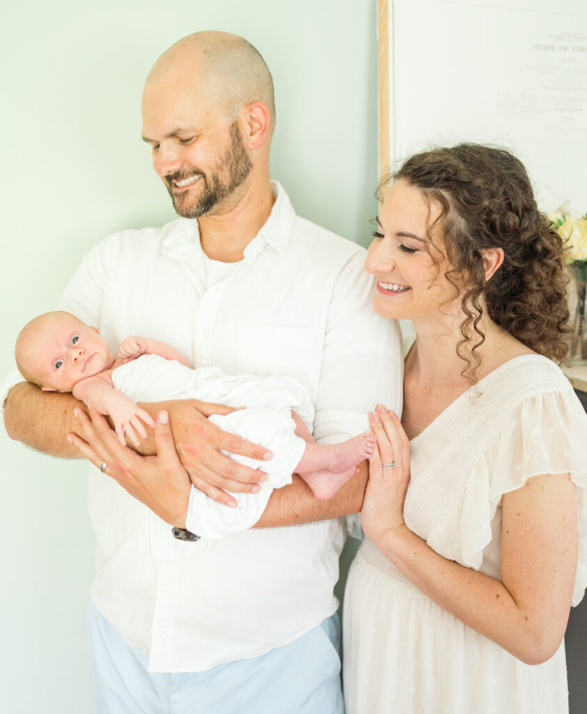 mom and dad smiling down at their brand new baby boy during lifestyle newborn photos at home in virginia beach