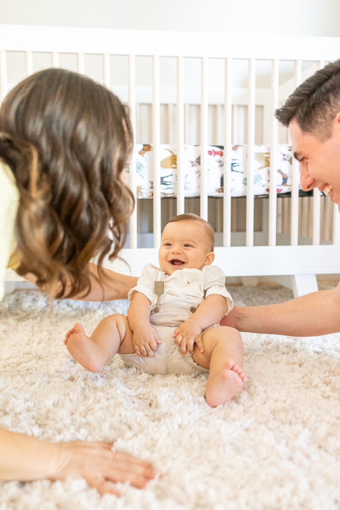 adorable baby boy sitting up and about to fall over with parents catching him and him smiling