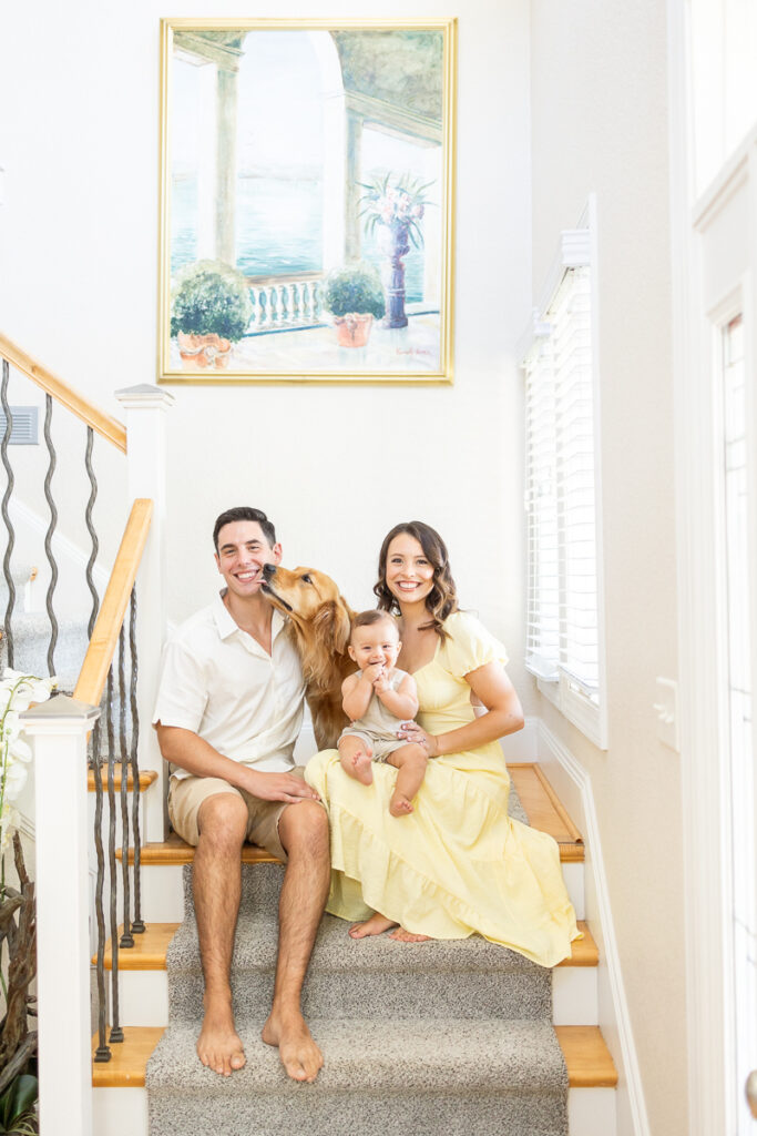 unique family photoshoot idea with family sitting on the stairs of their home, dog kissing dad while baby is overjoyed and laughs playfull during at home family photos