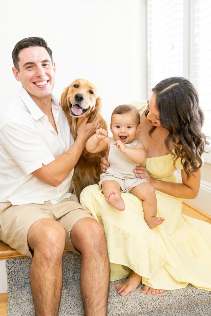 gorgeous family of 3 with golden retriever sitting on the stairs smiling and enjoying time together during family photos at home in moyock nc