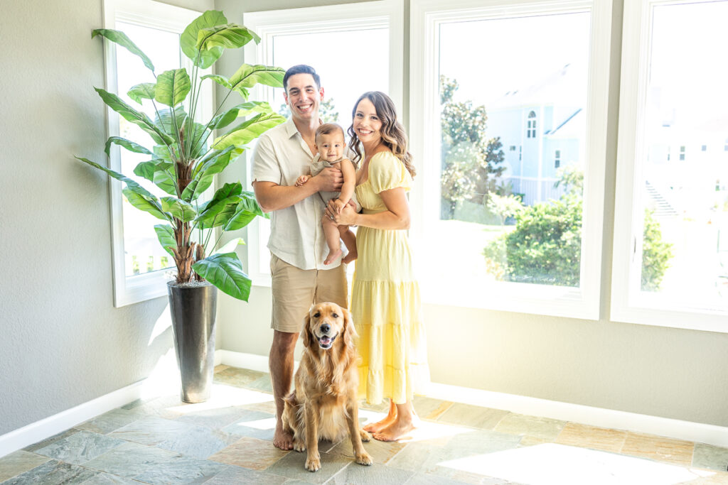 gorgeous family of 3 with golden retriever poses for smiling photo in their home with gorgeous golden light spilling in the windows. 