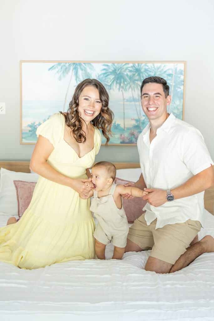 mom dad and baby smiling for family photos in their room during lifestyle family portraits at home