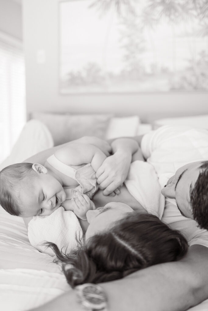 black and white family photo of baby and mom and dad snuggling in bed during family photos in their home