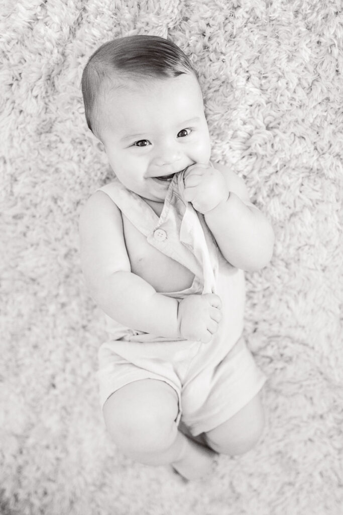 adorable black and white image of 7 month old baby smiling while laying on the carpet of his nursery