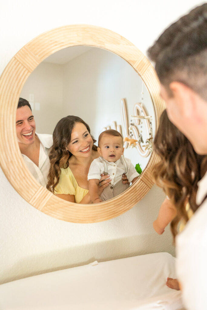 mom and dad smiling in the mirror with their 7 month old baby boy smiling during their in home family photos 