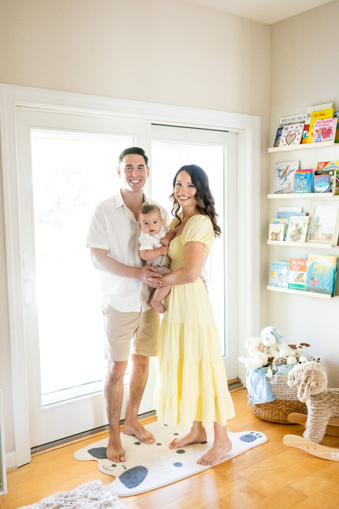 family of mom dad and baby smiling at camera during in home family portraits at clients home in the nursery