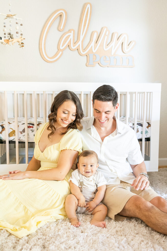 baby boy smiling at camera during at home family photos with. mom and dad smiling at him