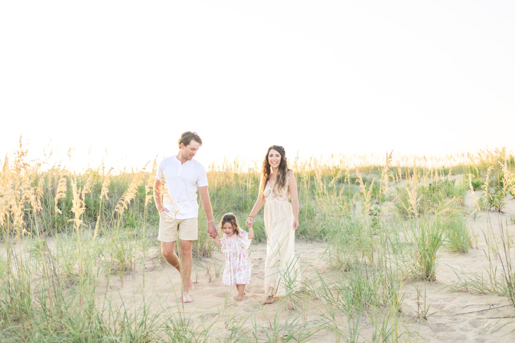 family of 3 walking in the dunes during their summer sunset beach photos in virginia beach