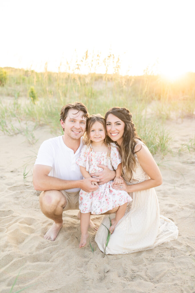 family of 3 smiling at the camera with mom having had professional hair and makeup done for their family photos