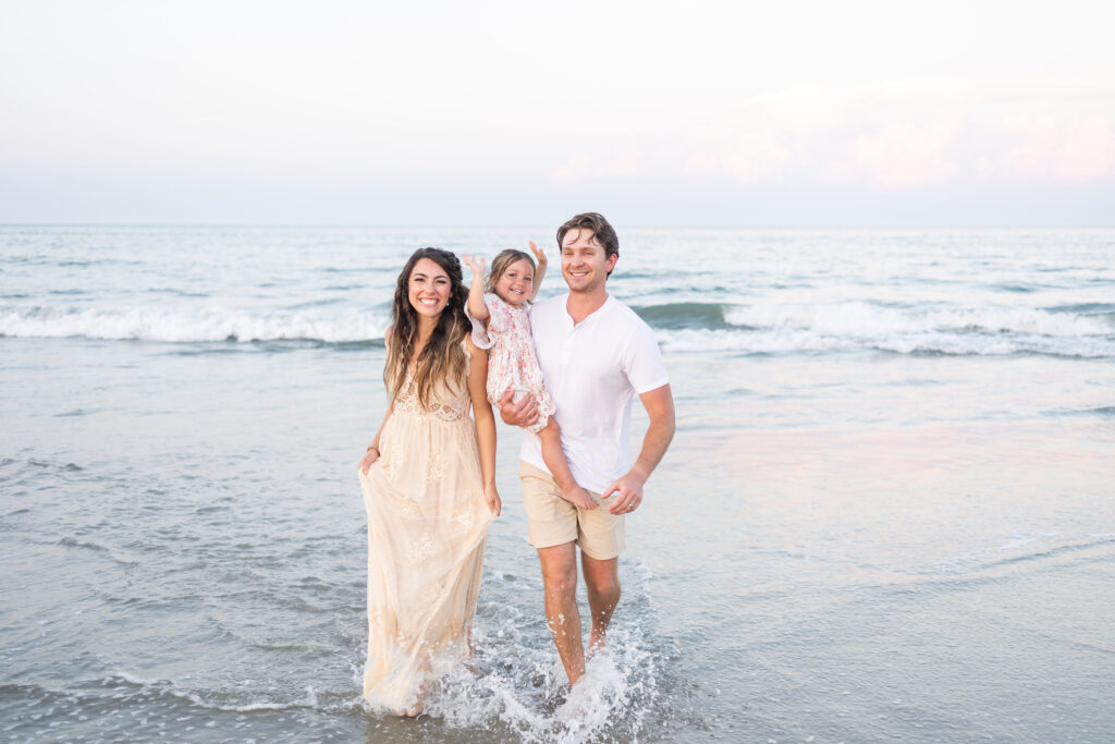 family of 3 running through the water and splashing during beach family photos 