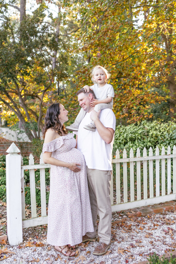 candid moment of mom holding her belly and dad holding toddler son on his shoulders during maternity photos 