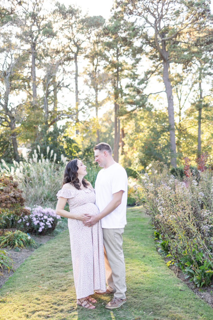 expectant mother and husband embracing during maternity photos at norfolk botanical gardens in norfolk, virginia 