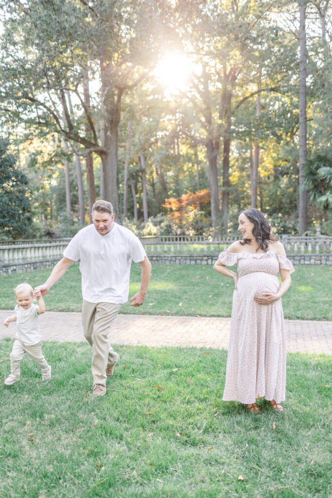 dad and toddler boy running and smiling around pregnant mom during maternity photos in virginia, usa 