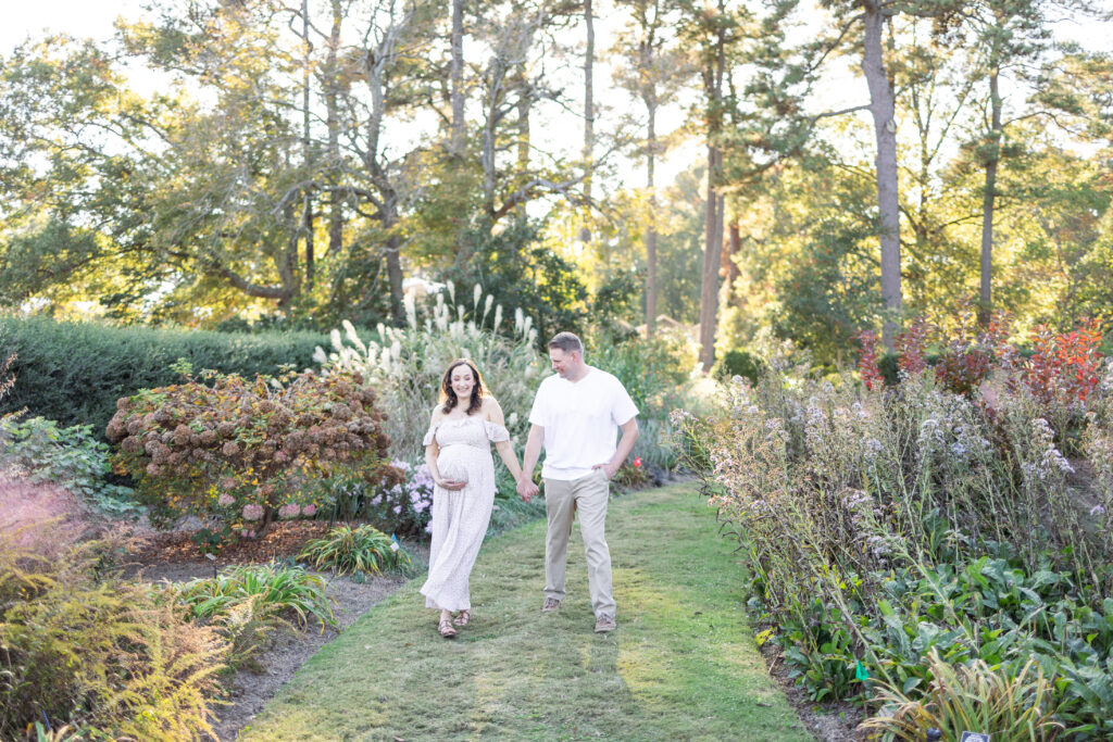 pregnant mom walking hand in hand smiling with her husband during maternity photos in norfolk, virginia