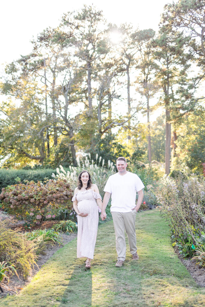 pregnant mom walking hand in hand smiling with her husband during maternity photos in norfolk, virginia