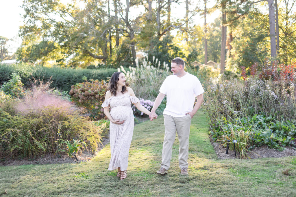 pregnant mom walking hand in hand smiling with her husband during maternity photos in norfolk, virginia