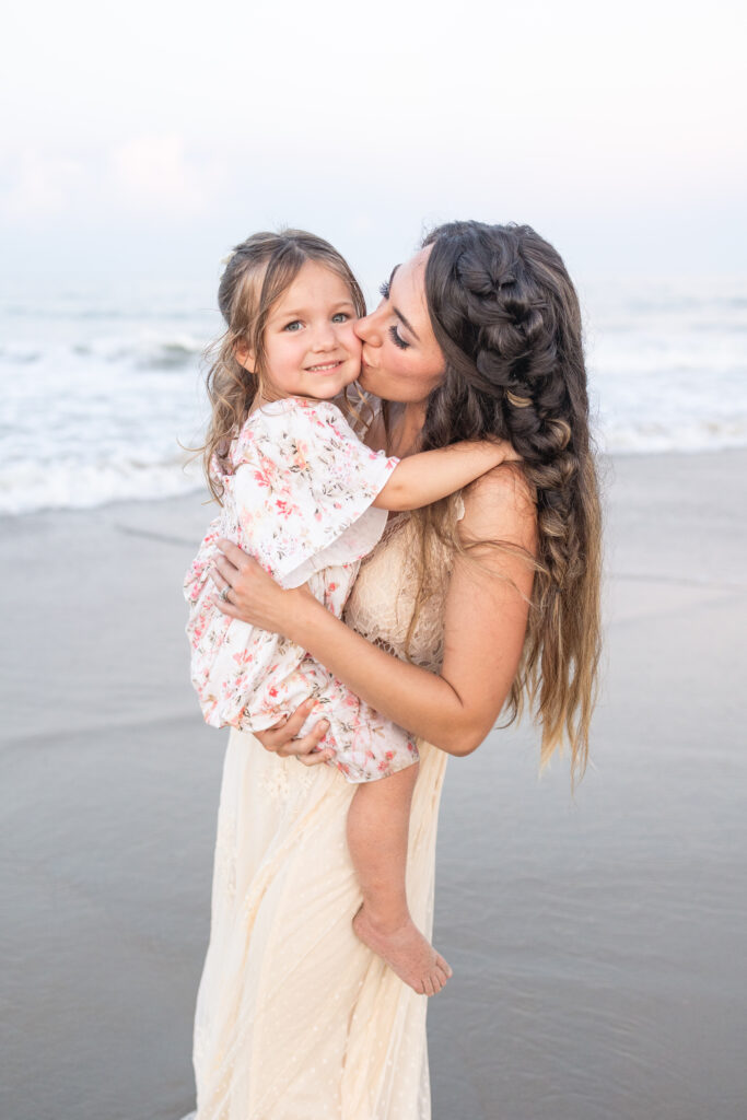 mom kissing her daughter during sunset photos on the beach in virginia beach