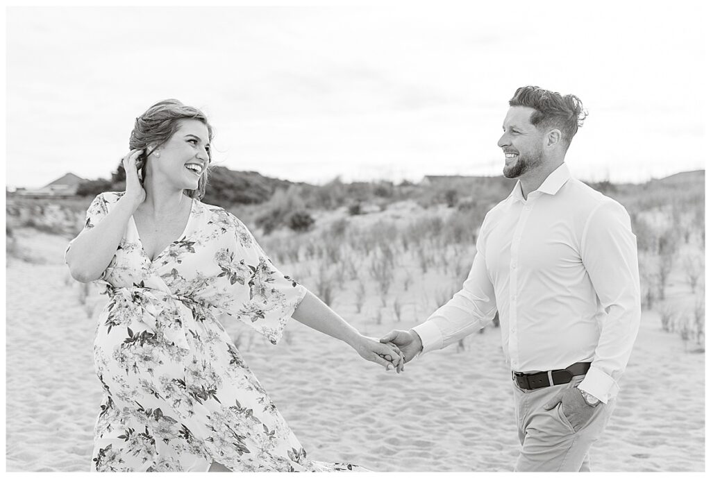 black and white photo of expectant mom and husband walking hand in hand during maternity photos on the beach