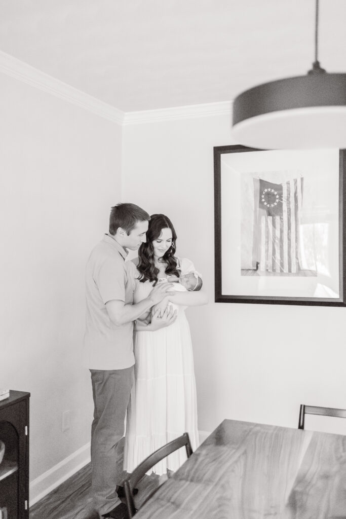 at home newborn photos in virginia beach showing a newborn baby being snuggled and held by mom and dad in their dining room