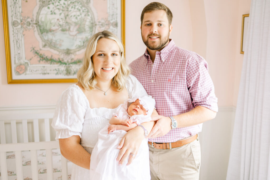 Mother holding her newborn baby girl smiling in a nursery with her husband