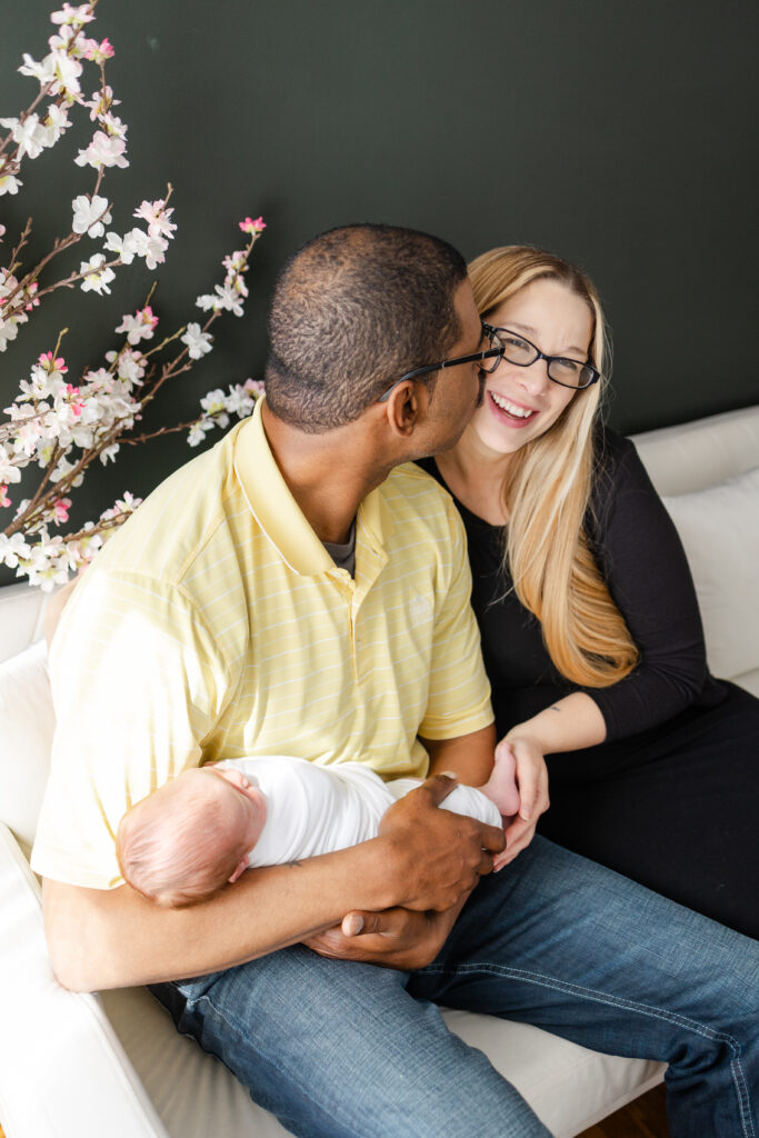 Sharing a sweet kiss with newborn baby during Newborn Photos In Virginia Beach