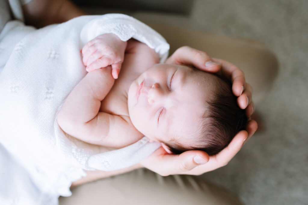 Baby being held wirh eyes closed by a Virginia Beach newborn photographer